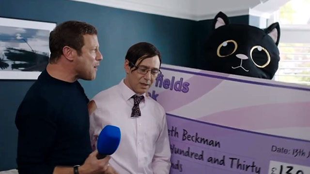 Inside No. 9 - Paraskevidekatriaphobia - Gareth Reece Shearsmith with Dermot O'Leary receiving giant check held by person in black cat costume