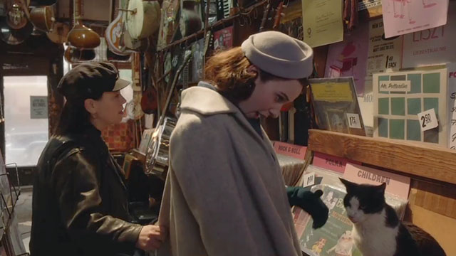 The Marvelous Mrs. Maisel - The Disappointment of the Dionne Quintuplets - Rachel Brosnahan and Susie Alex Borstein looking at albums in The Music Inn with tuxedo cat